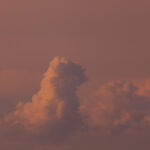 English: Wide shot of a sky at sunset or sunrise, featuring warm orange and pink-toned clouds, with one prominent cumulus formation. Estonian: Lai kaader päikeseloojangu- või päikesetõusuajast, kus on näha soojades oranžides ja roosades toonides pilvi, mille seas on üks silmapaistev rünkpilve formatsioon