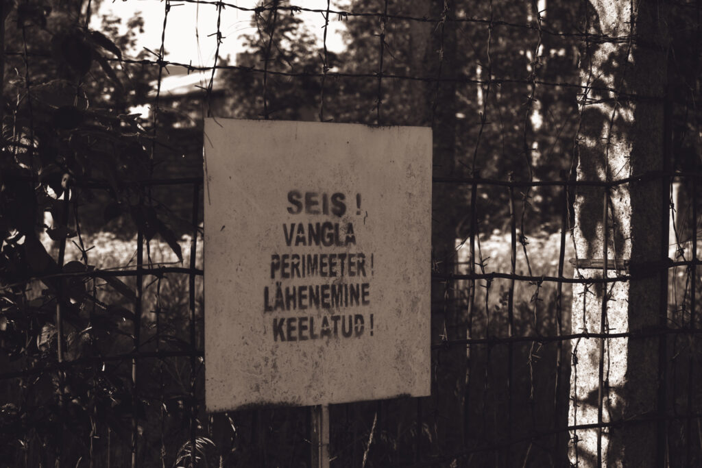 English: A weathered warning sign in Estonian reading "STOP! PRISON PERIMETER! APPROACH FORBIDDEN!" seen through a barbed wire fence, at Murru Prison, Estonia. Estonian: Ilmastikust kulunud hoiatussilt eesti keeles "SEIS! VANGLA PERIMEETER! LÄHENEMINE KEELATUD!", nähtud läbi okastraataia Murru vanglas, Eestis.