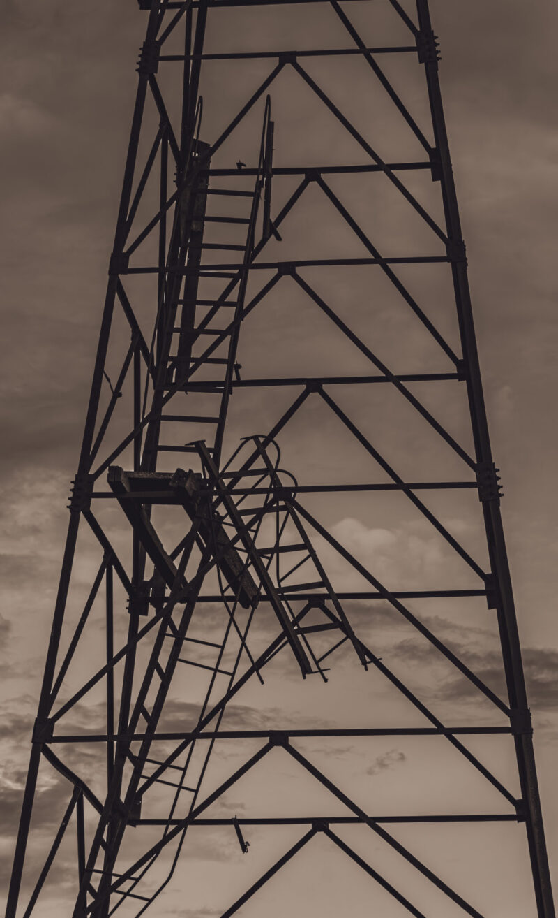A derelict watchtower standing in a decaying building, captured amidst overgrown vegetation and worn-out structures / Hõõguv vaatetorn lagunevas hoones, jäädvustatud üle kasvanud taimestiku ja kulunud struktuuride keskel