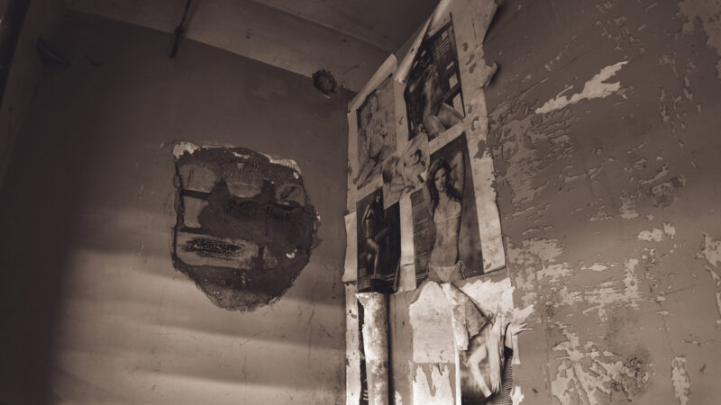 English: Dilapidated room in an abandoned Estonian building, featuring walls with peeling paint, a large hole, and old, tattered pin-up style posters. Estonian: Lagunenud tuba mahajäetud Eesti hoones, kus on seintel kooruv värv, suur auk ja vanad, rebenenud pin-up stiilis plakatid.