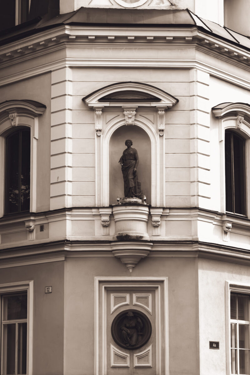 English: Corner of an old building in Tallinn Old Town featuring a statue in an arched niche, decorative windows, and classical architectural details. Estonian: Vana hoone nurk Tallinna vanalinnas, millel on kaarjas niššis kuju, dekoratiivsed aknad ja klassikalised arhitektuurilised detailid.