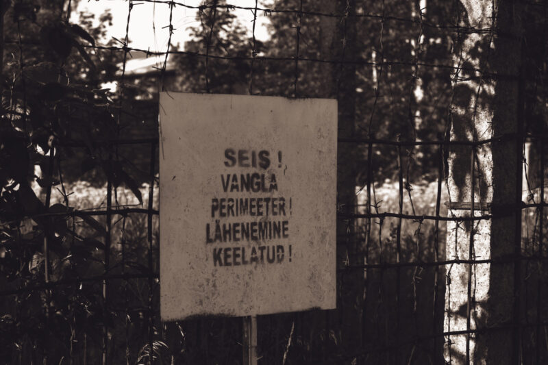 English: A weathered warning sign in Estonian reading "STOP! PRISON PERIMETER! APPROACH FORBIDDEN!" seen through a barbed wire fence, at Murru Prison, Estonia. Estonian: Ilmastikust kulunud hoiatussilt eesti keeles "SEIS! VANGLA PERIMEETER! LÄHENEMINE KEELATUD!", nähtud läbi okastraataia Murru vanglas, Eestis.