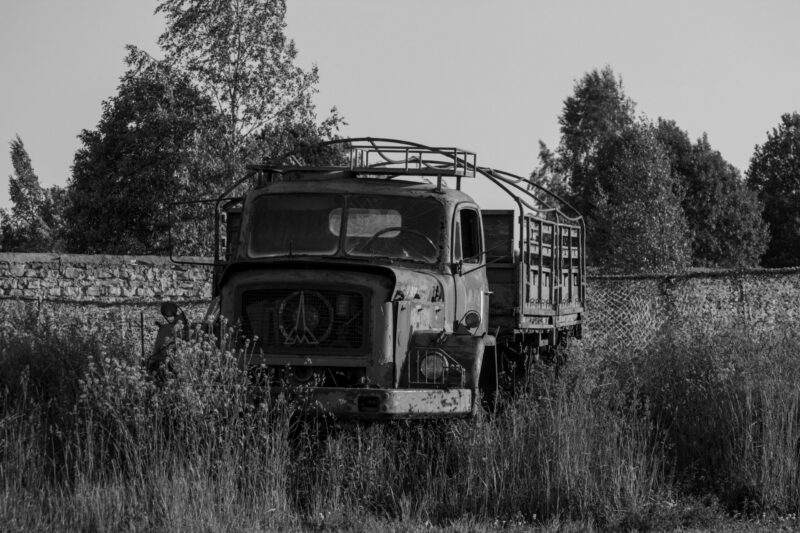 English: Black and white image of an old, abandoned Magirus Saturn or similar heavy-duty truck, overgrown with weeds, parked near a stone wall at Murru Prison, Estonia. Estonian: Mustvalge pilt vanast, mahajäetud Magirus Saturni või sarnase raskeveoki tüüpi veoautost, mis on umbrohuga kaetud ja pargitud kivimüüri lähedale Murru vanglas, Eestis.